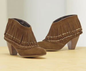 Brown suede ankle boots with fringe and gold accents, set on a wooden surface.