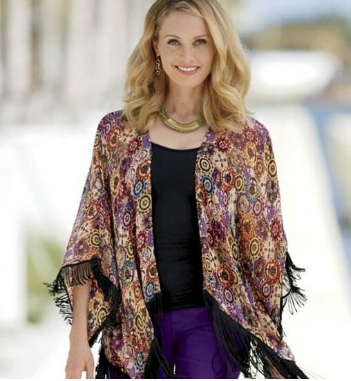 Woman in multi-color fringe duster over black top and purple jeans