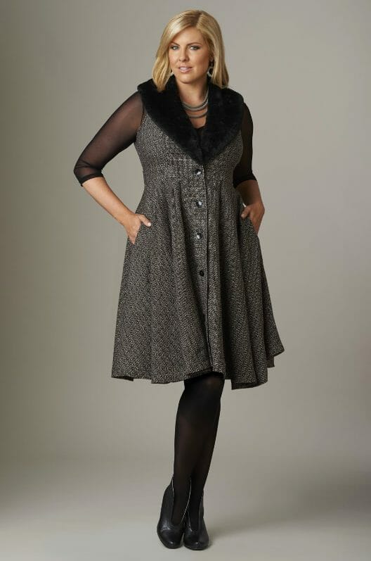 Woman wearing a black faux fur vest dress, black nylons and black booties