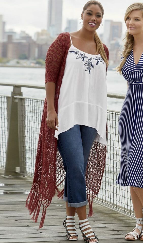 Woman in cropped jeans, white gladiators and a white open-knit crochet top under a paprika duster