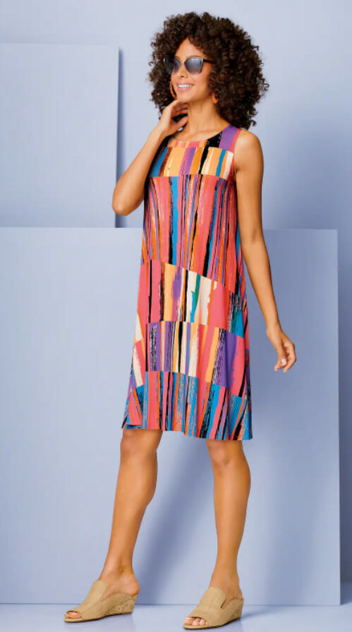Model in a colorful, patterned dress and sunglasses poses against a light blue background, exuding a stylish summer vibe.
