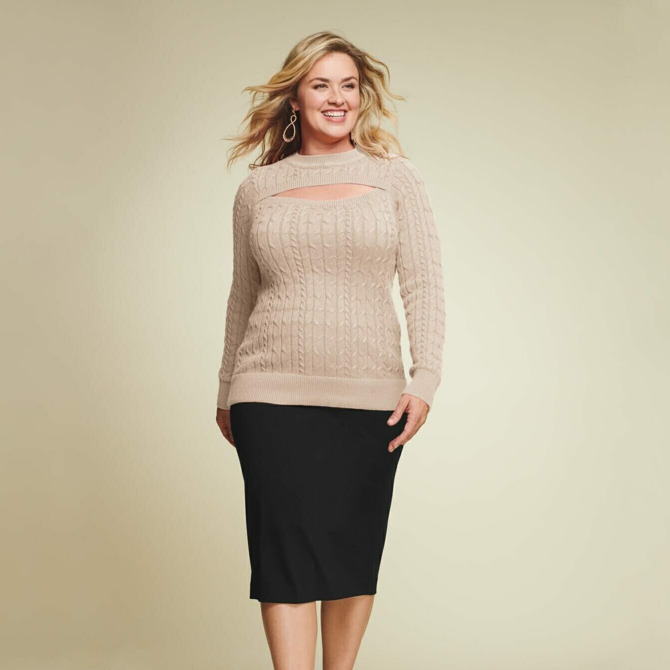 plus size model wearing a tan sweater with a black skirt.