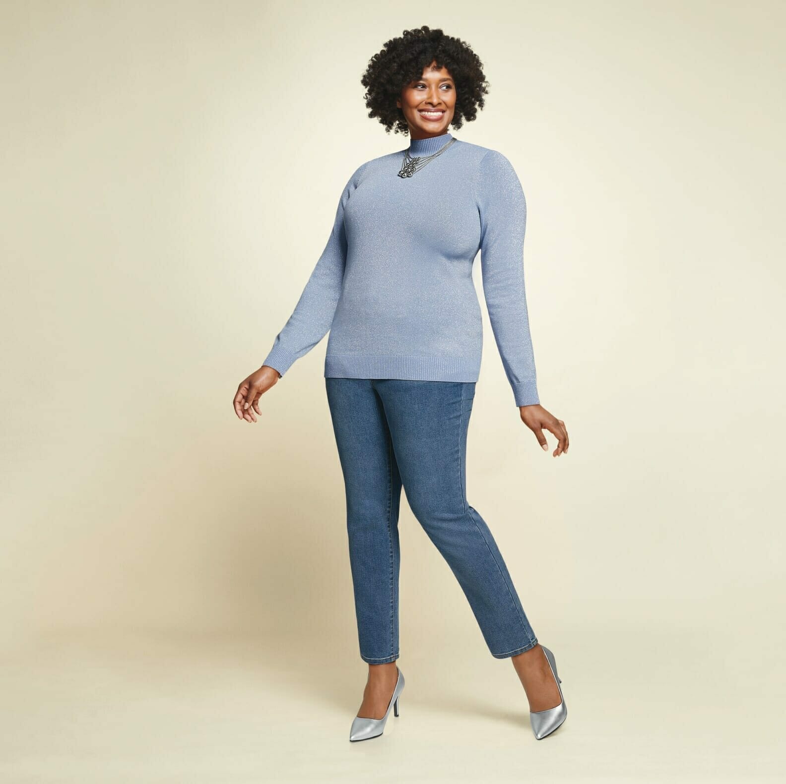 Plus size model wearing blue sweater with jeans and silver metallic heels.
