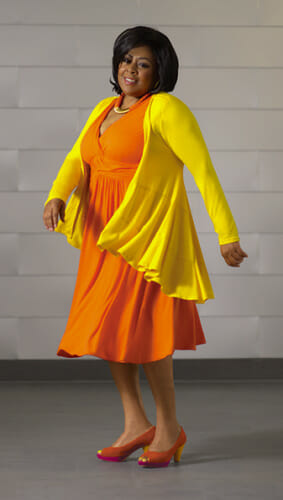 Woman in yellow jacket over orange A-line dress and orange pumps