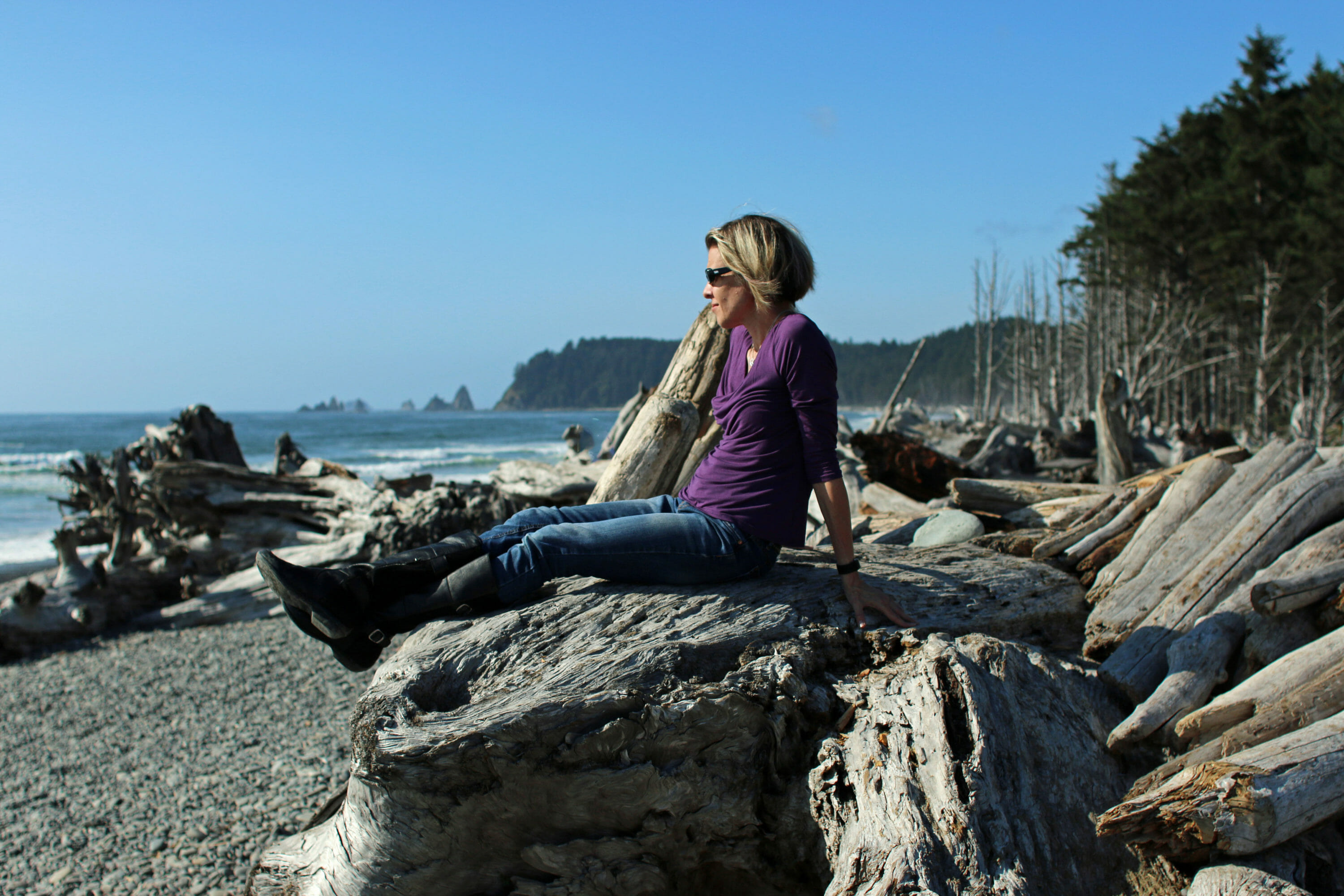 woman sitting on ocean jetty wearing purple top and jeans