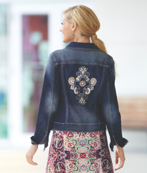 woman wearing an embroidered jean jacket over multi-color print dress