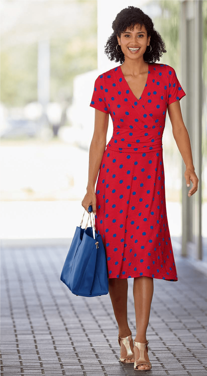 woman in red and blue polka dot dress, carrying a solid blue tote and wearing gold, heeled sandals