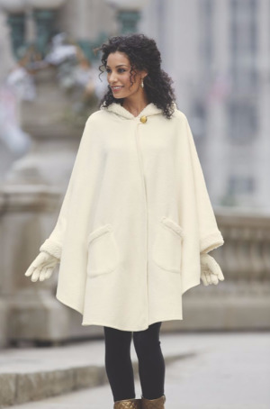 Woman wearing a white cape coat, matching gloves, black leggings and gold boots
