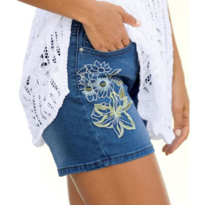 woman wearing blue jean shorts with embroidered flowers on leg and white crochet top