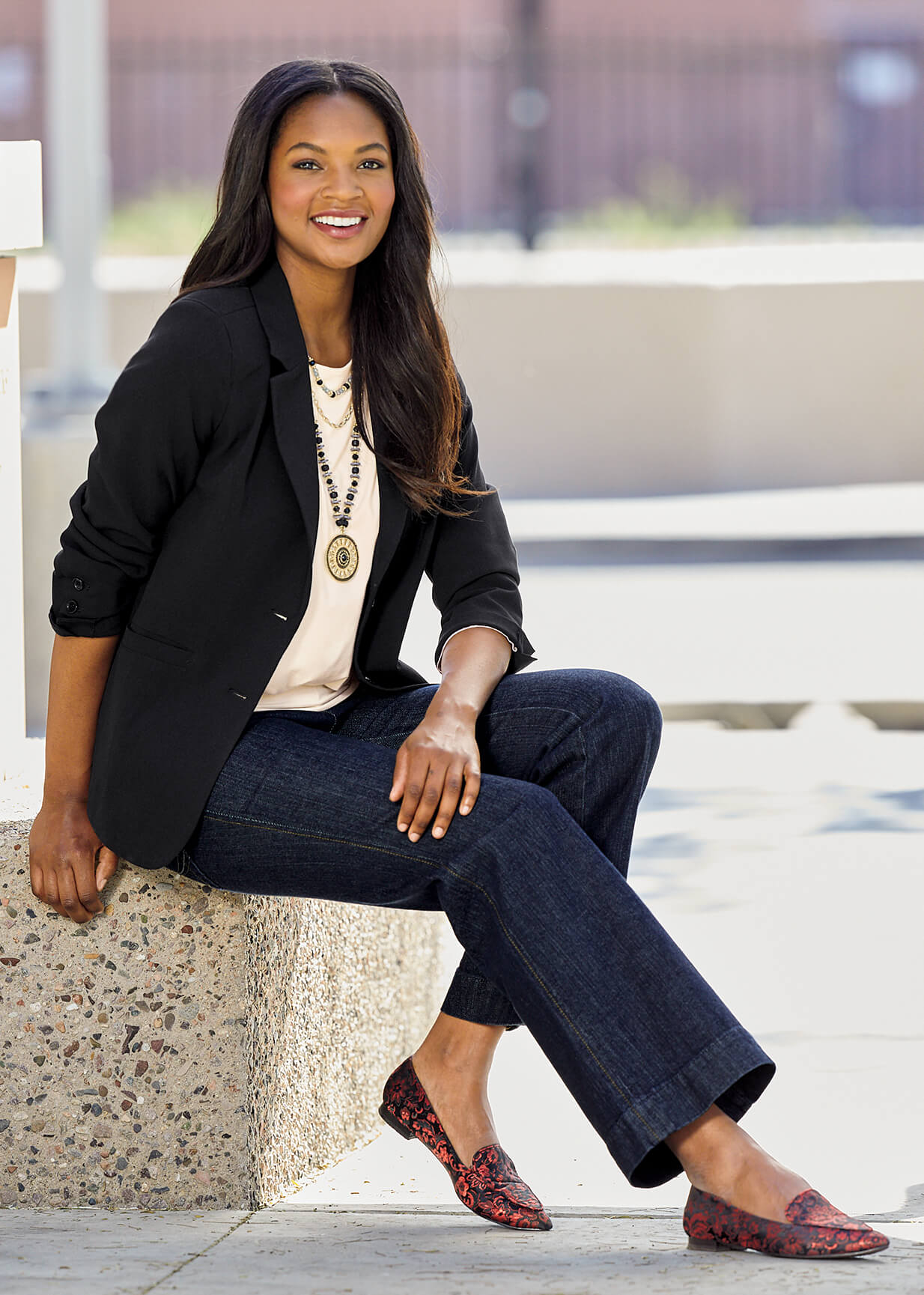 Woman sitting down wearing a black blazer with jeans and high heel shoes