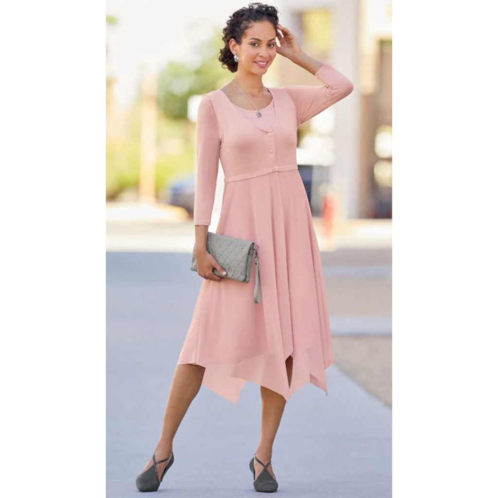Woman in soft pink, empire waist dress and matching vest with open mesh skirt and hankie hem