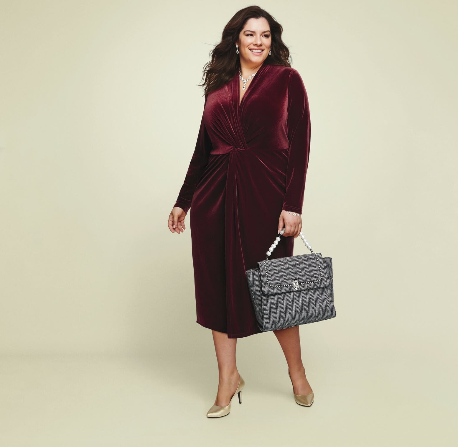plus size model wearing a burgundy velvet dress with gold pumps and a grey bag