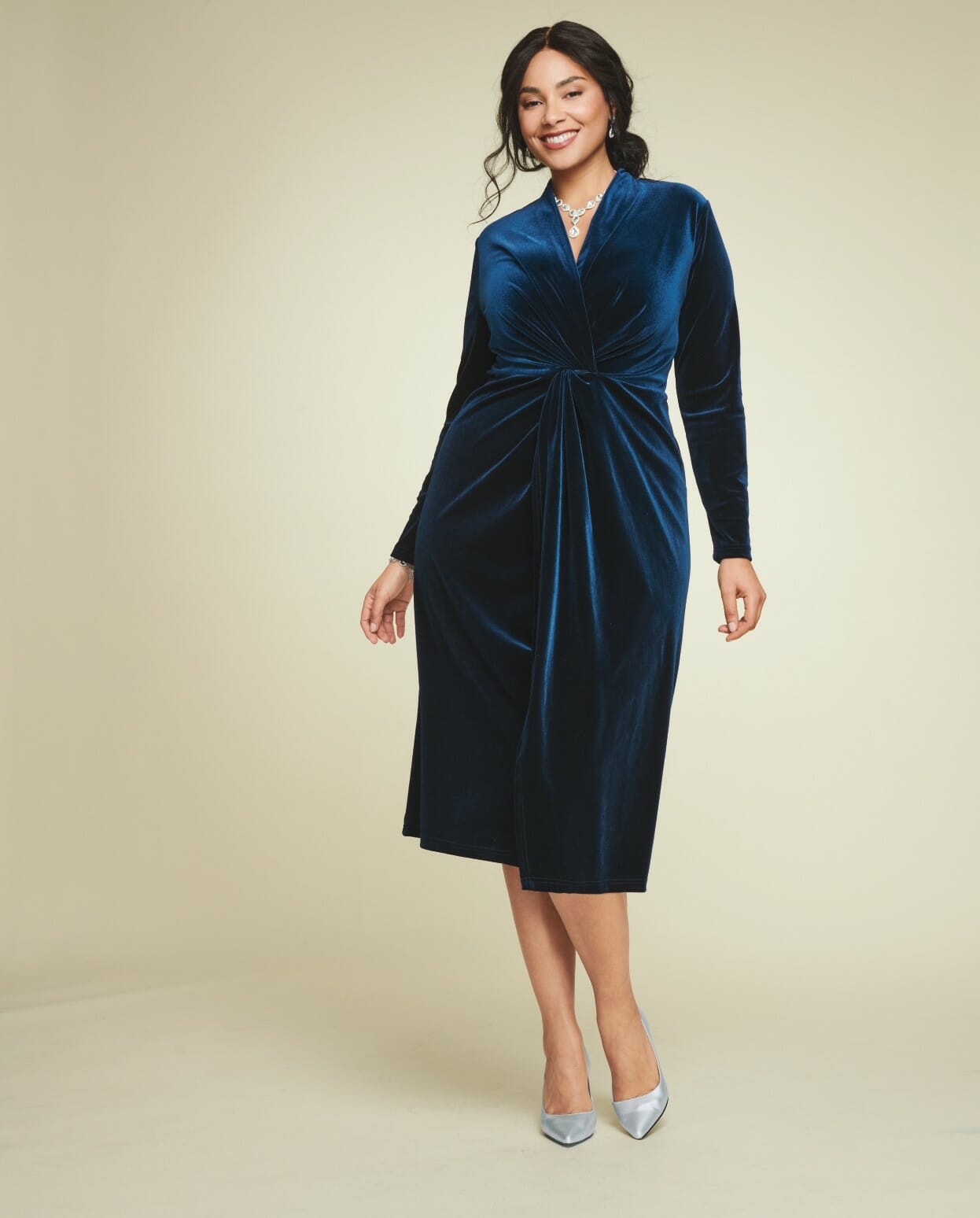 plus-size model wearing a navy long-sleeved dress with jewelry with silver heels.