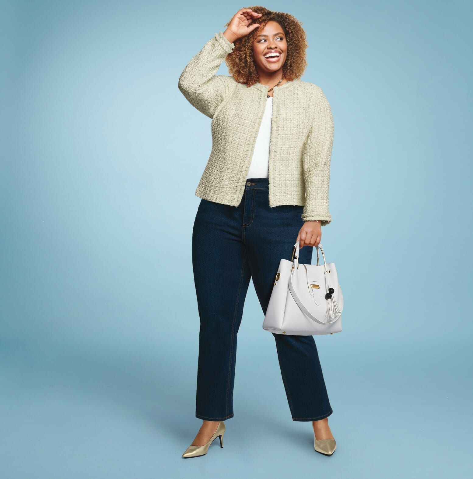plus-size model wearing a cream jacket with jeans and a white purse.