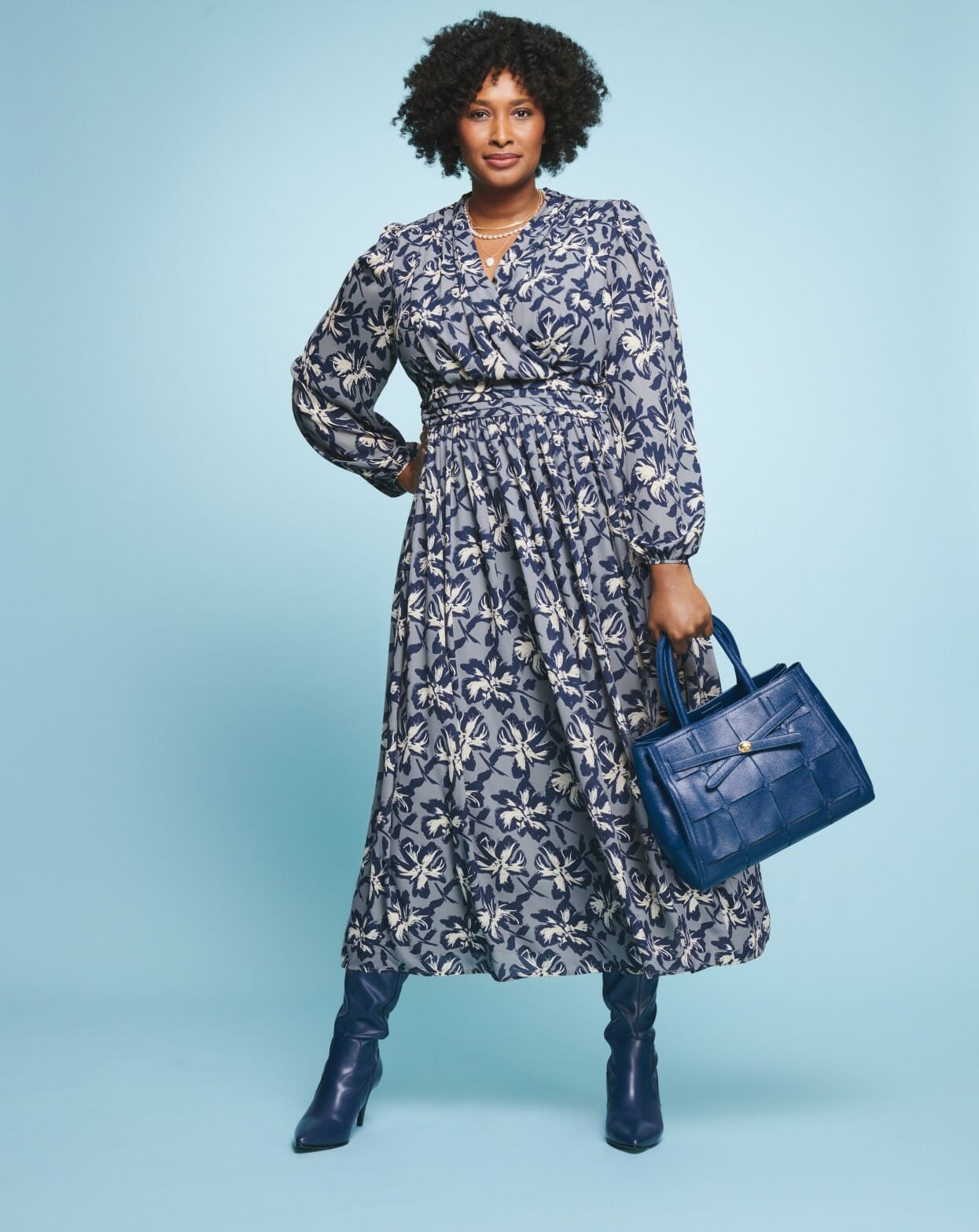 plus size model wearing a floral blue dress holding a blue purse.