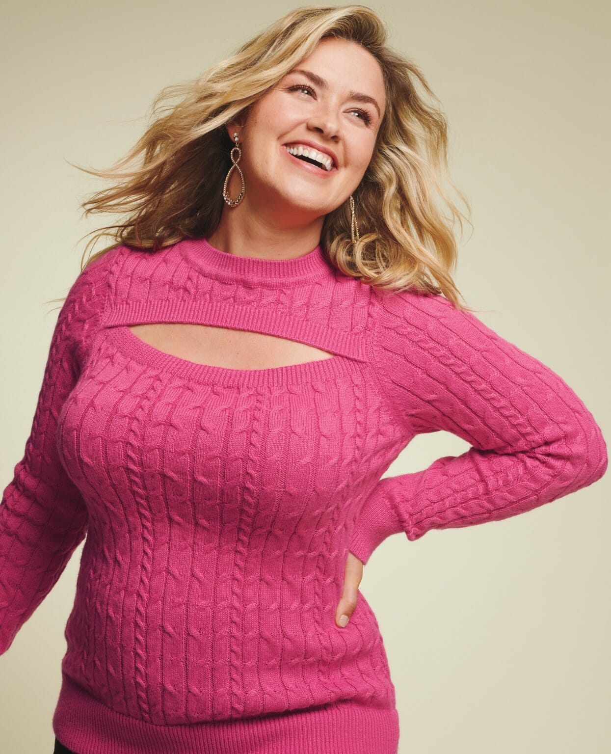 plus size model wearing a pink sweater with earrings.