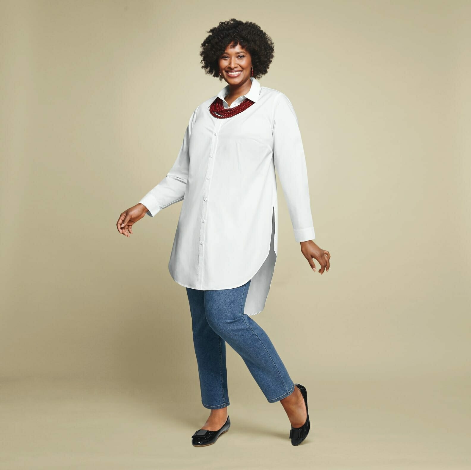 Plus size model with a white long-sleeve blouse with jeans and a red beaded necklace.