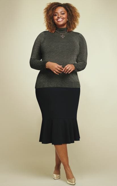 Black plus size model wearing a shimmery grey sweater and a black skirt with gold pumps. she smiles as she looks at the camera